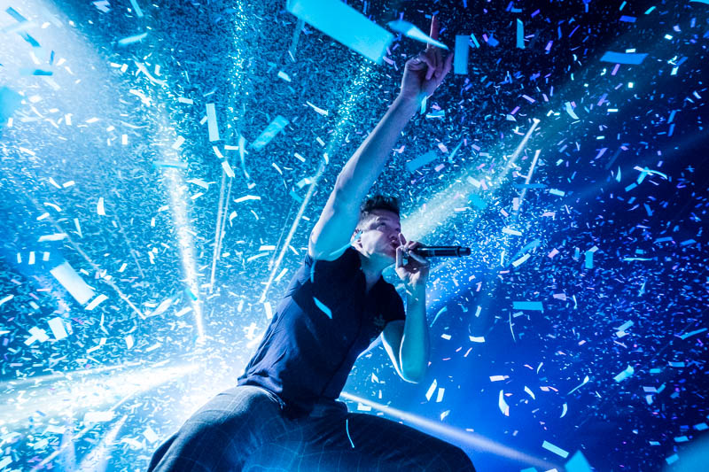 Imagine Dragons performing beneath blue stage lights and falling confetti — photograph by Tom Di Maggio